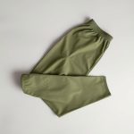 Olive green yoga pants men neatly folded, minimalist top-down view on neutral background, yoga gear for men.