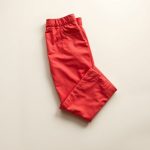 Flat lay of organic cotton white flare pants in red, neatly folded on a neutral surface.