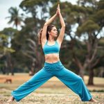 A woman in sky blue wide leg yoga pants and yoga bra performing a yoga pose in an Australian park.